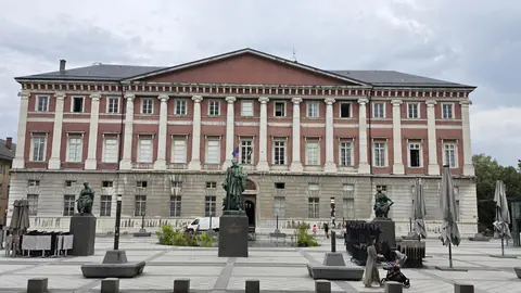 A pink and white front across the square, bronzes standing guard.