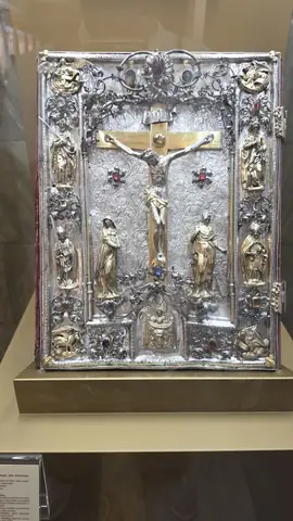 A silver crucifix under glass, worked to within an inch of its life.